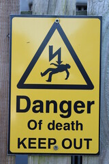 Danger of death keep out sign in yellow with black text and silhouette of man being electrocuted
