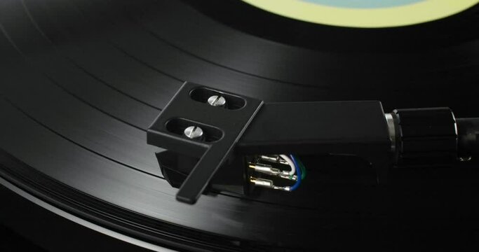 Extreme turning closeup of tonearm headshell on spinning vinyl record with colorful label