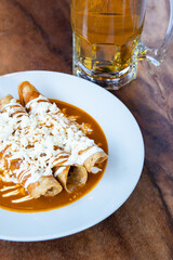 Drowned Mexican flutes, traditional Mexican food with red sauce. Drowned tacos. Traditional Mexican food. Mexican food on wooden background. Traditional Mexican food concept.