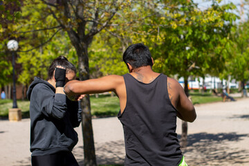 Female boxer sparring with her trainer in outdoor  sportive training. Latin coach and white Hispanic girl