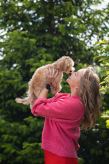 a woman in a pink jacket holds a Maltipa puppy in her arms