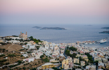Fototapeta na wymiar Panoramic View of Ermoupolis City in Syros Island, Greece at Sunset. Nice Seascape and Greek Horizon View of Aegean Sea. Traditional White Houses, Villas, Church and Port. 