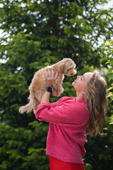 a woman in a pink jacket holds a Maltipa puppy in her arms