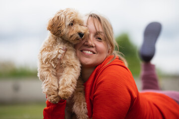 a blonde woman in a red sweater plays with a Maltipu dog