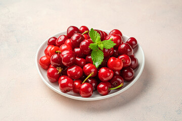Red, juicy cherries and mint in a plate on a pink background.