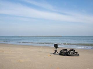 action camera lay beside the sandle on the sand beach with blue sky background