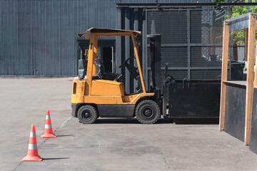 Hyster branded yellow forklift truck on the street in the warehouse. Two traffic cones, with white and orange stripes on gray asphalt.