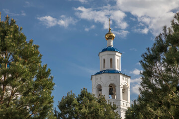 Fototapeta na wymiar A beautiful white tower with a dome among the trees. An old church. Sunny day. Harmony with nature