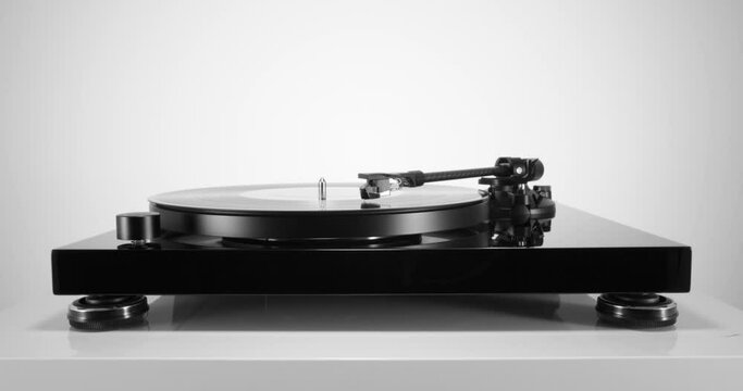 Front view of black turntable with spinning vinyl record on white table. Static full body shot