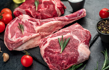 Assorted raw beef steaks. Tomahawk steak and ribeye steaks on stone background