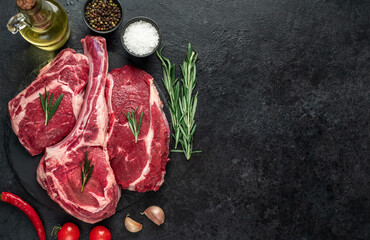 Assorted raw beef steaks. Tomahawk steak and ribeye steaks on stone background with copy space for your text