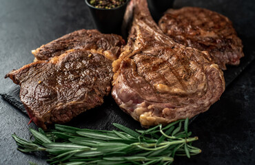 Variety of grilled beef steaks. Grilled tomahawk steak and ribeye steaks on stone background