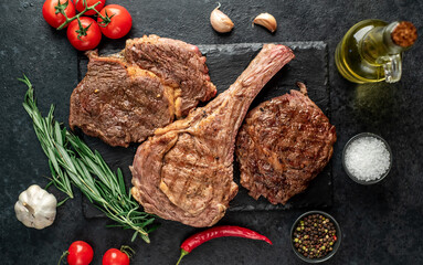 Variety of grilled beef steaks. Grilled tomahawk steak and ribeye steaks on stone background