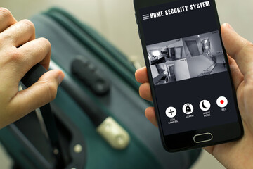 Person in an airport with his suitcase holding his smartphone and observing the wirelessly connected home security cameras. Protected home concept.