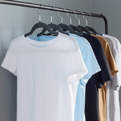 T-shirts of neutral colors on  black hanger against  gray wall