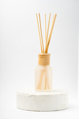 Fototapeta na wymiar Aroma bottle glass and wooden sticks staying on cement white podium on white background