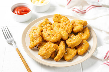 Chicken nuggets in a plate, ketchup and cheese sauce on a light background. Fast food closeup	