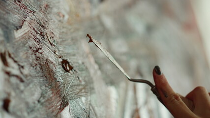 Unknown girl creating artwork in art studio. Woman hand holding palette knife.