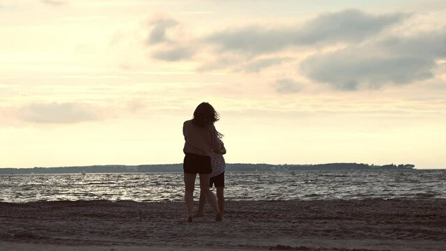 Slow motion video of happy young mother dancing and jumping with her teen daughter on baech during sunset