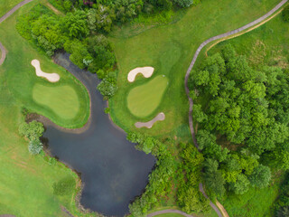 In the photo we see a wooded area, a meadow, a pond. Bright green color of trees, bushes, grass. Sunny day. There is no one in the photo. View from above. Shooting from a drone.