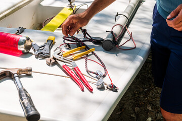 Sailboat repair and  maintenance: close up of tools , shackels and hands in use to refit the boom on a a small dingy's .