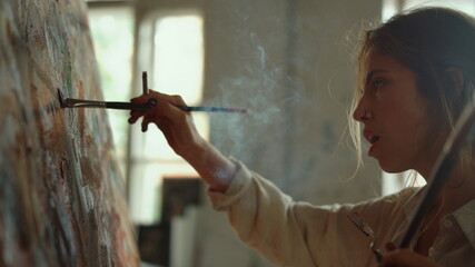 Inspired woman creating masterpiece indoors. Painter exhaling smoke in studio.