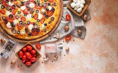 In the left corner of the photo, we see pizza on a wooden plate, as well as ingredients laid out around it. Light background. There is an empty space for your insert. High angle view.