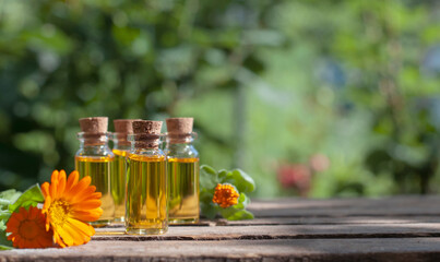 essential oil bottles with fresh calendula on the nature blurred background with copy space	 - obrazy, fototapety, plakaty