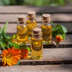 essential oil bottles with fresh calendula on the wood table