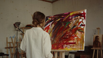 Back view of female artist painting indoors. Creative painter drawing in studio.
