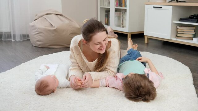Cute baby and older boy lying with smiling mother on carpet in living room. Parenting, children happiness and family relationship