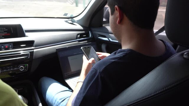a man working from the car as a co-pilot using his phone and laptop returning from a vacation trip in the daytime in 4k