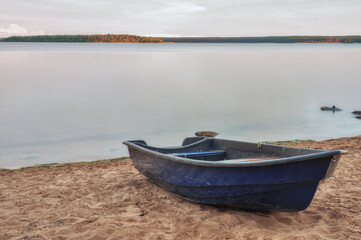 Blue plastic boat on the sandy beach of the lake.
