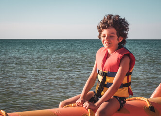 Little boy in waistcoat enjoying water activities on banana boat at the black sea.