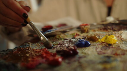 Fototapeta na wymiar Creative woman using brush indoors. Unknown painter mixing oil paints in studio.