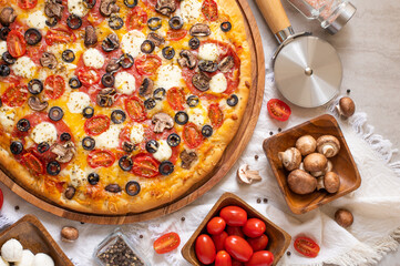 A beautiful composition of pizza, as well as bright, colorful ingredients - tomatoes and mushrooms. In the upper right corner there is a photo-knife for cutting pizza. Light background.
