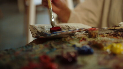 Creative woman mixing paints at workplace. Unknown painter using brush indoors.
