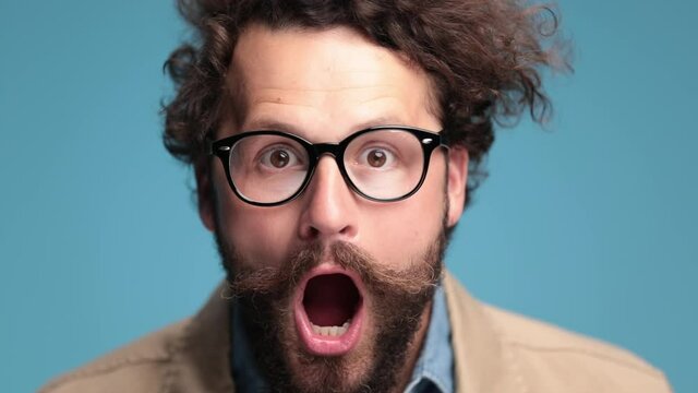 shocked casual man with moustache and eyeglasses opening mouth and being surprised, laughing and being happy on blue background in studio