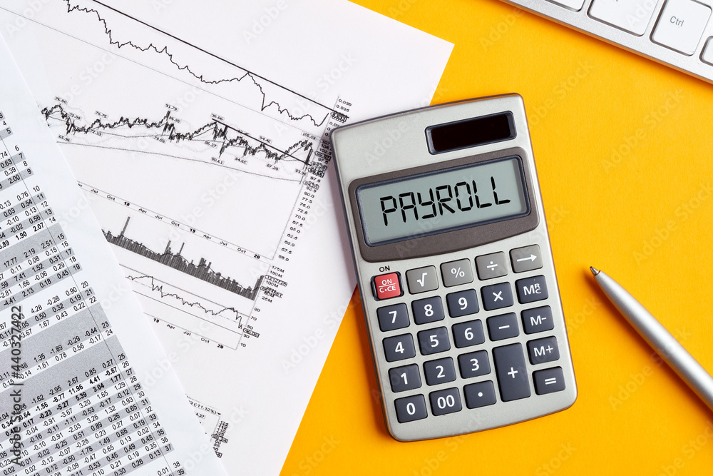 Poster the word payroll on calculator display screen with business office desktop. calculating or analyzing
