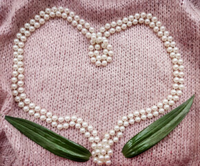 background soft thick woolen fabric of gentle pink color with small sequins with cones and white pearls in the shape of a heart for valentine's day or Valentine's day and a green leaves 