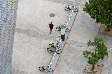 A man walks past a dock with several shared bicycles ate Parque das Nações neighbourhood. Located by the Tagus river, the modern buildings host mostly services and office spaces. 