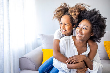 Attractive woman and little girl sitting on comfortable couch at home. Young mother talking...