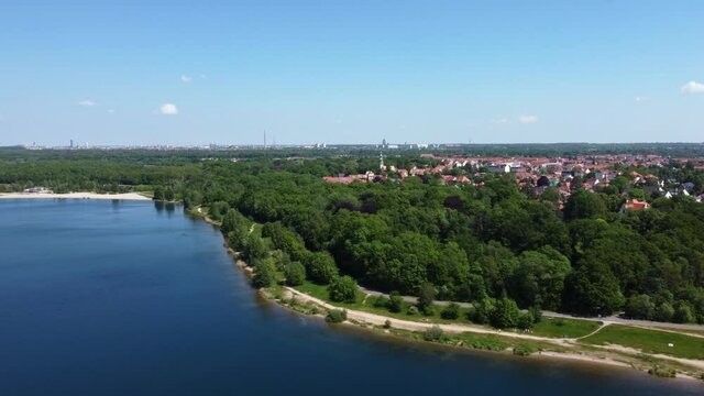 Drone flight with panoramic view of a lake and surrounding forest. In the background: the skylines of the cities of Markkleeberg and Leipzig (German: Cospudener See)