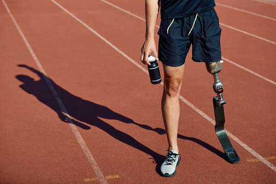 Unrecognizable runner with leg prosthetic standing on running track. On his shadow he is seen celebrating success as he stands with raised arm.