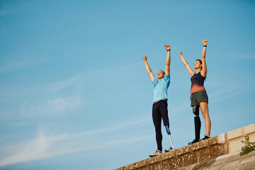 Disabled athletic couple with prosthetic legs celebrating their achievement while standing with...