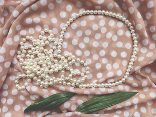 Beige delicate natural background for cosmetics and beauty fabric fashionable textile dotted with white pearls and perfume with green leaves nature and beauty femininity
