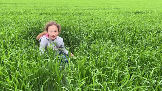 4k Cute small girl sitting on a green grass, smiling and looking around.