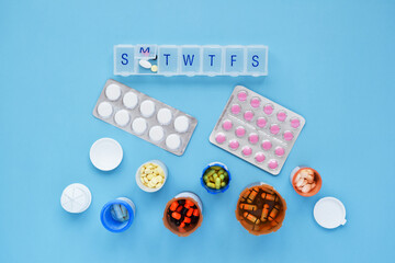 Variety of prescription medication with weekly organizer on blue background