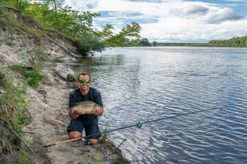 Feeder fishing. Fisherman with big bream fish in hands and tackle at wild river shore