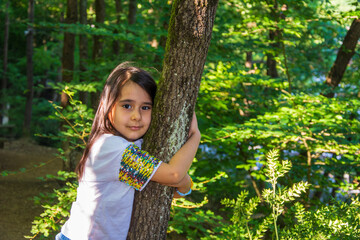 Little girl hugging a tree in the forest and smiling towards the camera